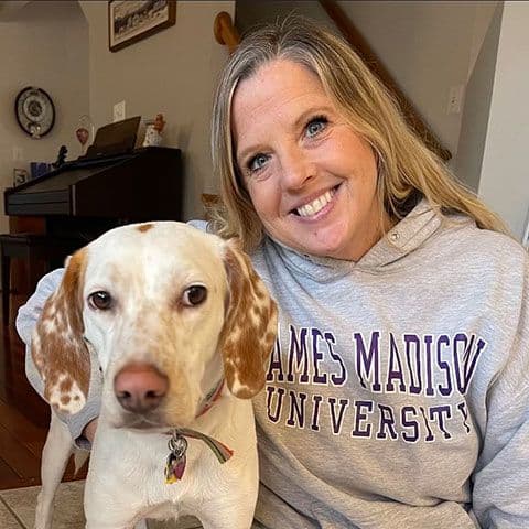 a white dog with brown spots with its owner looking at the camera